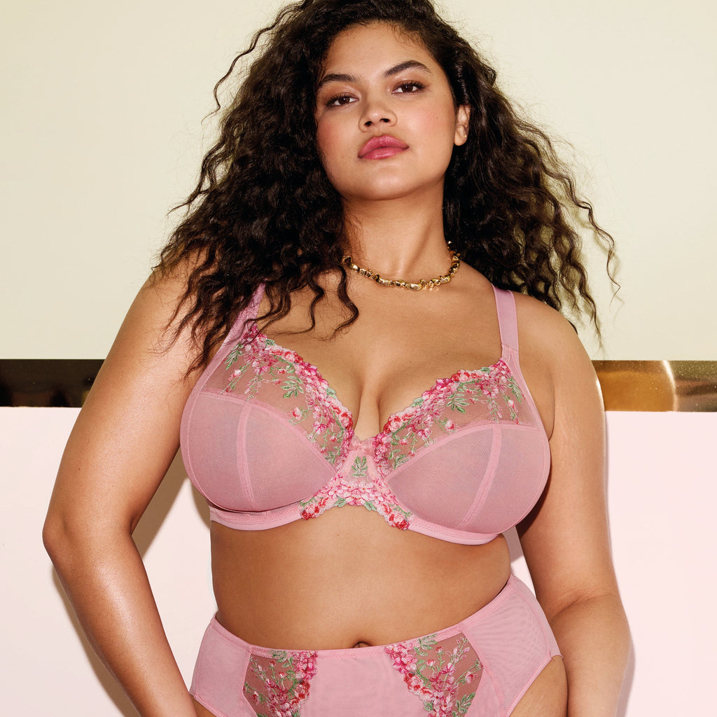 Woman wearing a pink lingerie set with floral details against a light green background
